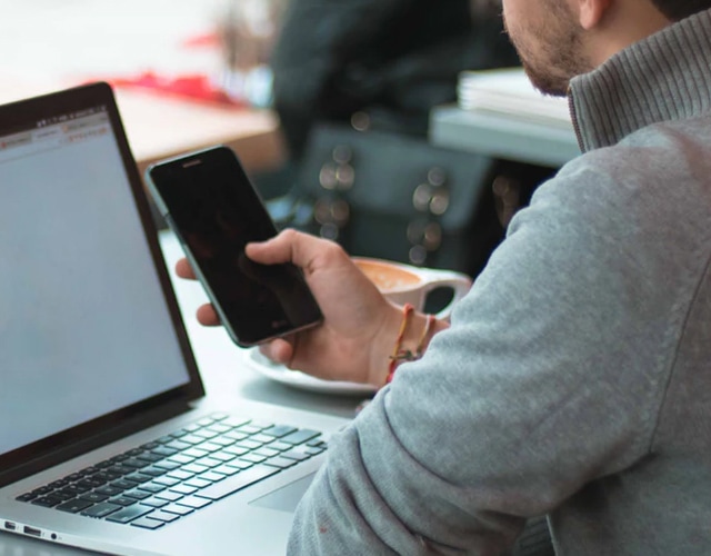 A man using his laptop and phone to communicate and schedule an appointment.