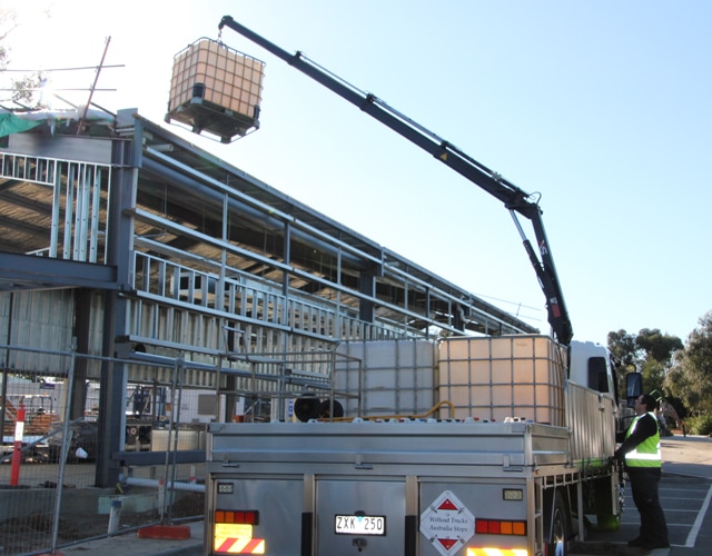 A truck equipped with a crane is lifting a container of toxic waste at a hazardous site.